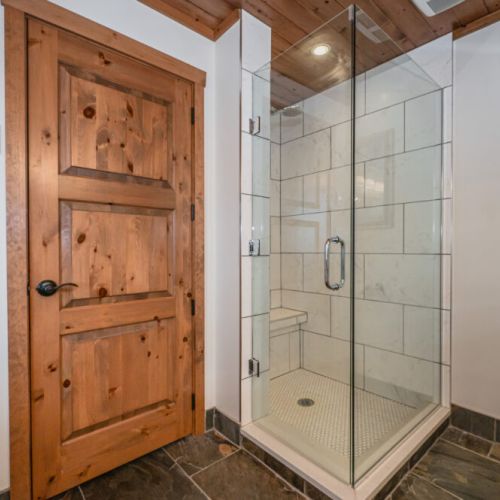 Step into Anchorage’s modern shower room, where simplicity and elegance are paramount. The glass enclosure reflects the clean lines and uncluttered design, complemented by the neutral tones of the tile work. A sturdy wooden door provides a touch of rustic charm, perfectly aligning with the property's post-and-beam architecture.