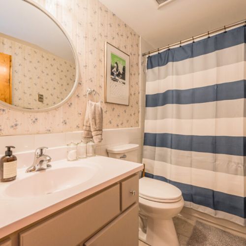 Freshen up in a bathroom that reflects the home's quaint charm, complete with a large mirror and a touch of vintage flair.