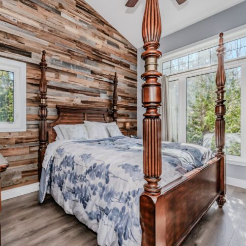 Rustic elegance meets comfort in this forest-view bedroom, featuring a stunning reclaimed wood accent wall and cozy four-poster bed—perfect for a serene lakeside retreat.