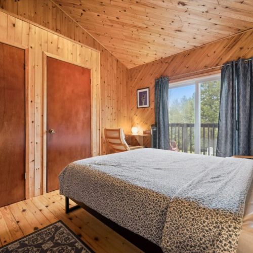 Bright and comfortable upstairs bedroom with a queen bed, natural light, and access to fresh air from the nearby balcony.