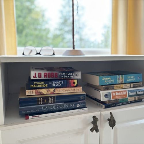 Reader’s Retreat: A bedside shelf holds a selection of books, inviting guests of The Louise to indulge in the pleasures of reading. With titles ranging from thrilling mysteries to tales of the wilderness, there’s a story for every reader to unwind with by the window, under the soft afternoon light filtering through, creating a perfect nook for book lovers.