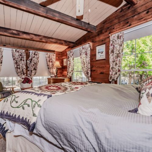 Bask in natural light and woodland views in this spacious bedroom. Featuring rustic charm, floral curtains, and a handcrafted quilt—perfect for tranquil mornings during your countryside or lakeside escape.