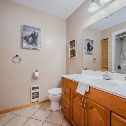 A clean and well-organized bathroom featuring a large mirror, and a wooden vanity. The space has a warm, natural feel with soft lighting and practical amenities.