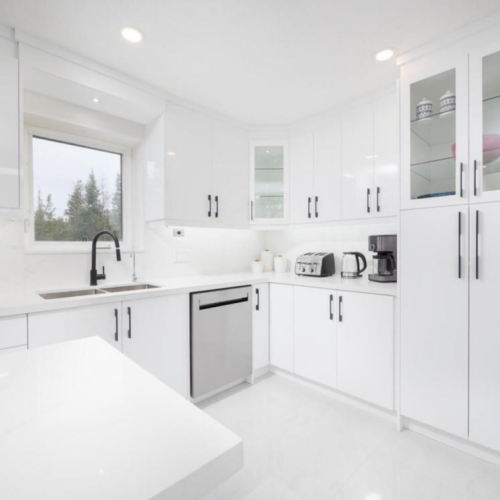 A sleek and contemporary kitchen featuring glossy white cabinetry, quartz countertops, stainless steel appliances, and a black faucet, enhanced by under-cabinet lighting and large windows for natural light.
