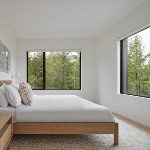 A minimalist bedroom with large windows, offering peaceful views of the surrounding greenery.