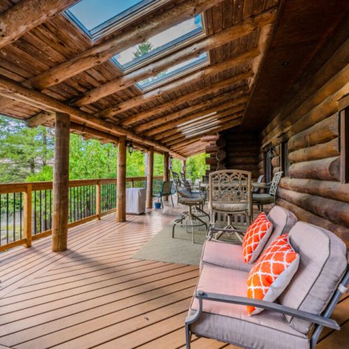 This cozy covered porch, complete with comfortable seating, invites you to unwind while enjoying the serene forest views and the rustic charm of the log cabin exterior.