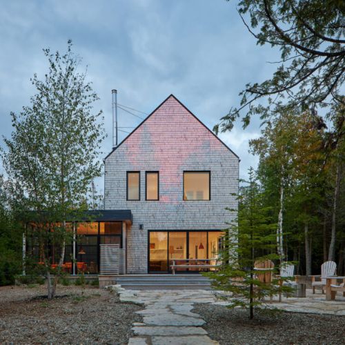 A picturesque cottage with a stone pathway, outdoor seating area, and a hint of the fireplace glow from inside.