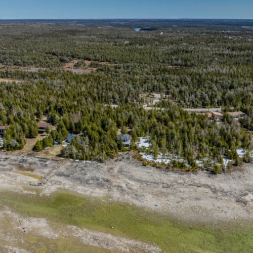 Expansive aerial view of your peaceful cottage escape, nestled between pristine forest and sparkling waters — the perfect nature retreat!