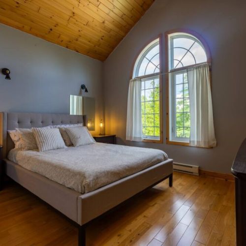 Evenings feel magical in this softly lit bedroom with dramatic windows and plush bedding—perfect for winding down in luxury.