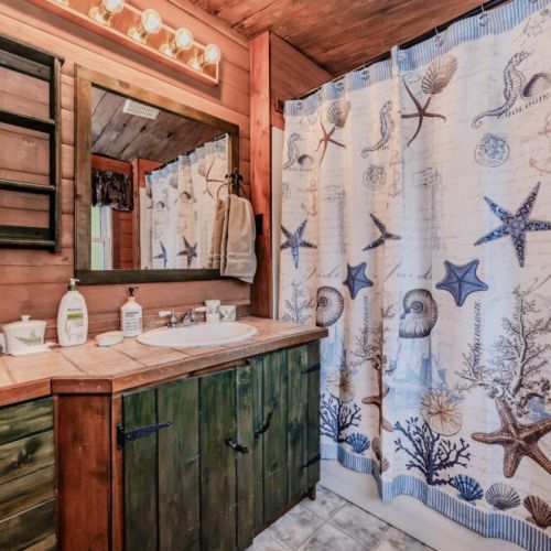 Refresh in this charming full bathroom, featuring a nautical-themed shower, rustic vanity, and warm wood finishes—perfect for relaxing nature escapes, weekend getaways, and family retreats.