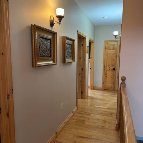Charming hallway with warm wood finishes and cozy lighting, leading to beautifully appointed bedrooms—perfect for a peaceful cottage retreat.