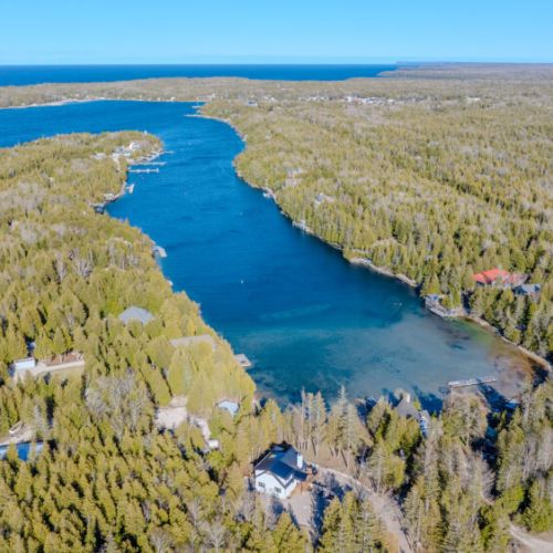 Aerial view of a tranquil lakeside inlet surrounded by forested shoreline and private residences—ideal for waterfront retreats and scenic vacation stays.