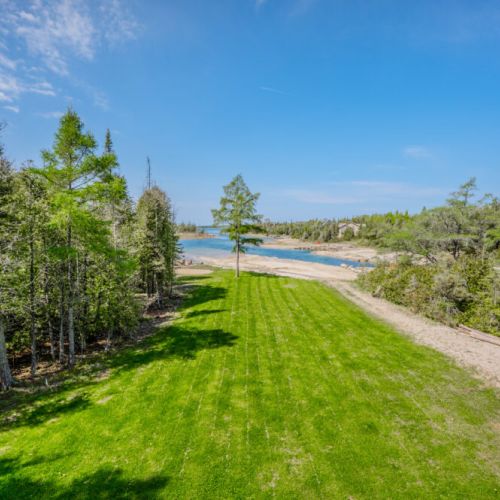 Enjoy the scenic beauty of this expansive green lawn that gently slopes down to a serene waterfront, providing a perfect spot for outdoor activities and picturesque views.