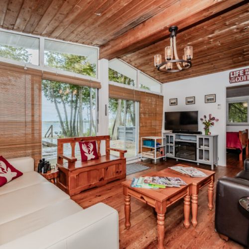 Relax in a charming lakeside living room with rustic wood accents, panoramic windows, and modern comforts—perfect for your cottage retreat.