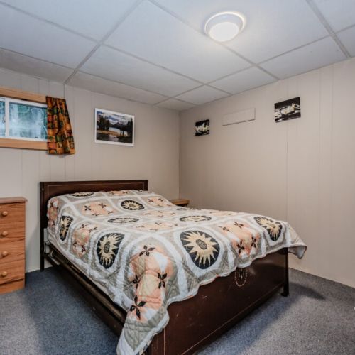 A second bedroom with simple decor, featuring a comfortable bed, dresser, and fan for added comfort.