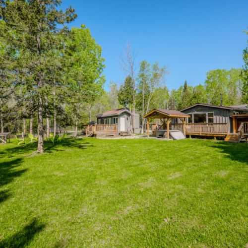 The expansive yard features lush green grass and is surrounded by trees