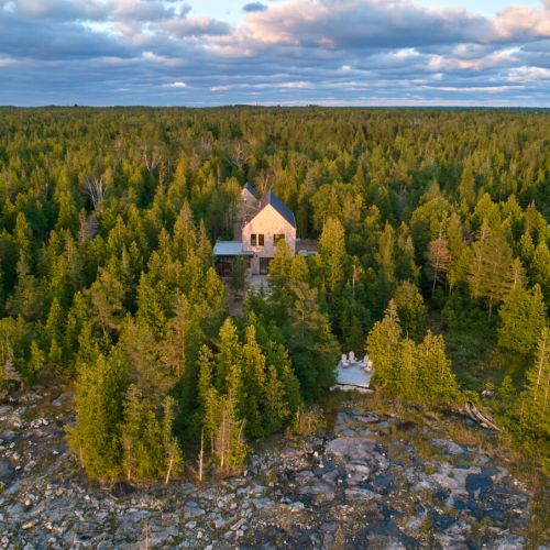 A serene view from above showcasing the cottage nestled among dense woods with beautiful rocky shores nearby.