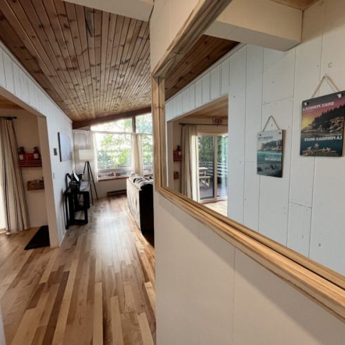 A bright hallway featuring a large mirror and wood-paneled ceiling, leading to the living area with abundant natural light and scenic views.