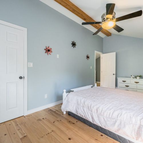 The spacious bedroom offers a cozy retreat with soft hues, a ceiling fan, and charming decor, perfect for a restful night's sleep.