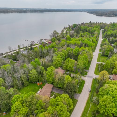 Charming lakeside road framed by lush trees and bayfront access—an ideal setting for peaceful walks and waterfront exploration.