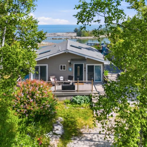 Nestled among mature trees, this charming waterfront cottage offers deck seating and lake views. Ideal for summer getaways, outdoor living, and unforgettable coastal cottage travel.