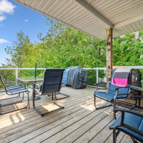 Spacious covered deck with glass railing, outdoor dining area, and BBQ, offering scenic lake views and a perfect spot for entertaining or relaxing in a peaceful natural setting.