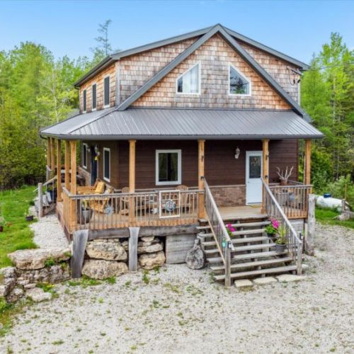 Nestled between trees, the cottage’s beautiful wood and stone exterior radiates warmth and charm. The gravel driveway leads up to the cozy wraparound porch—perfect for quiet mornings and evening chats.