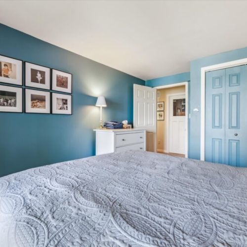 A warm and welcoming bedroom that invites you to settle in, featuring classic cottage decor, family photo gallery wall, and soft, layered linens.