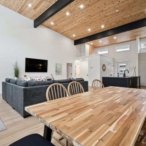 Open-concept great room featuring wood ceilings, exposed beams, and seamless flow between kitchen, dining, and living spaces.