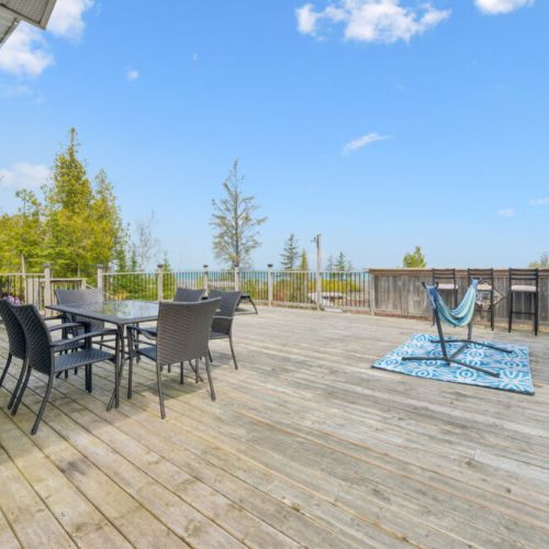 Expansive waterfront deck with outdoor dining, lounge seating, and panoramic bay vistas.