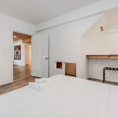 Chic and functional bedroom featuring cozy bed, luggage rack, and custom desk nook—ideal for travelers combining relaxation and productivity.