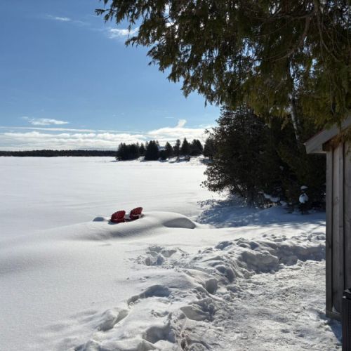 Two red chairs waiting for warmer days by the frozen lake.