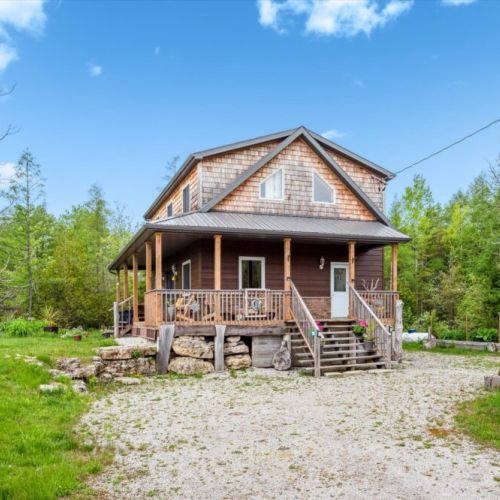Front view of Sunny Meadow Place—surrounded by trees and flowers, this cozy cottage welcomes you to relax and reconnect.