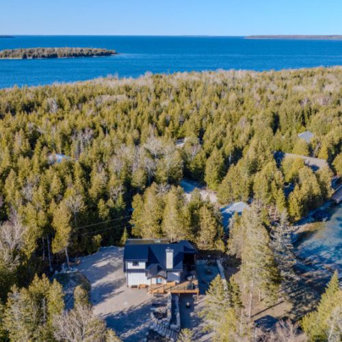 Breathtaking aerial view of your private cottage oasis nestled in the trees, just steps from crystal-clear waters. The ultimate vacation rental for nature escapes and waterfront adventures.