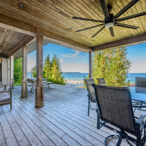 A spacious wooden deck with comfortable seating, ceiling fan, and a dining area overlooking a scenic waterfront view.