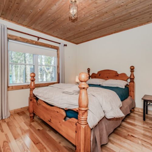 Charming bedroom with wood ceilings and tranquil forest views—an inviting space for restful getaways in Bruce Peninsula cottage country.