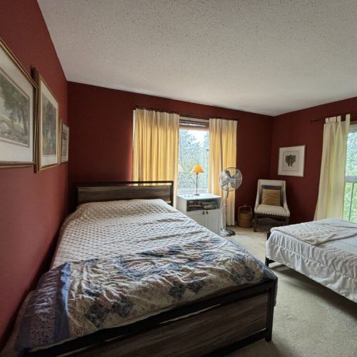 Classic Elegance: The bedroom is a picture of classic elegance, with a richly hued wall providing a warm backdrop to a traditional bed ensemble. Vintage landscape paintings adorn the wall, adding an artistic touch and a sense of serenity to the room, while the ample natural light enhances the space’s welcoming atmosphere.
