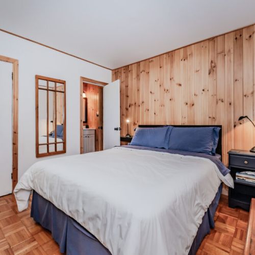 Serene cottage bedroom with wood-paneled walls and a cozy queen bed — the perfect retreat after a day at the beach or on the trails.