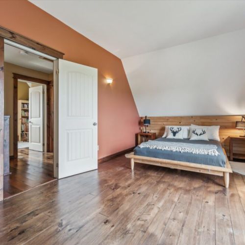 Spacious upper-level bedroom with a queen bed, minimalist decor, angled ceiling, and handmade headboard crafted from local wood.