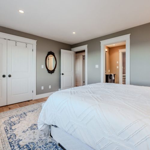 A spacious bedroom with a large window showcasing beautiful water views, featuring simple yet elegant furnishings.