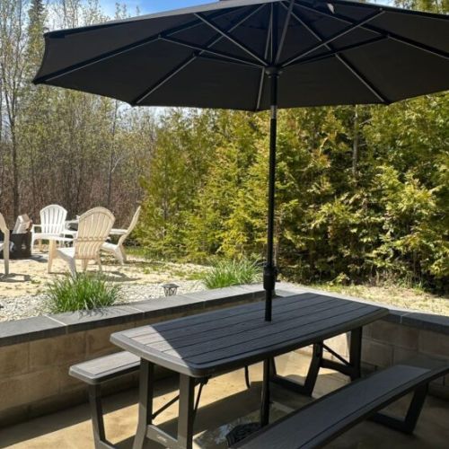 Outdoor dining area with picnic table, umbrella, and cozy fire pit seating nearby.