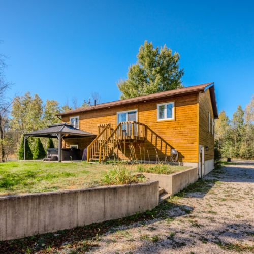 A stone path leads to a fire pit with seating, while a covered patio and wooden steps provide access to the home.