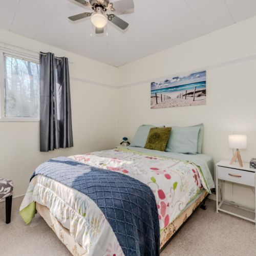Bright and airy guest bedroom with queen bed, soft tones, and large windows—an inviting space for unwinding after a day at the lake.