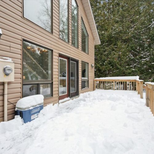 Main-level exterior with large windows, deck access, and snowy forest views