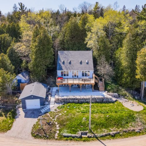 Picturesque front view of the cottage, nestled amidst greenery with a spacious deck overlooking the lake.