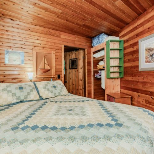 Relax in this serene bedroom, featuring a handcrafted quilt, rustic wood paneling, and nautical accents—perfect for peaceful nature escapes, family vacations, or romantic countryside getaways.