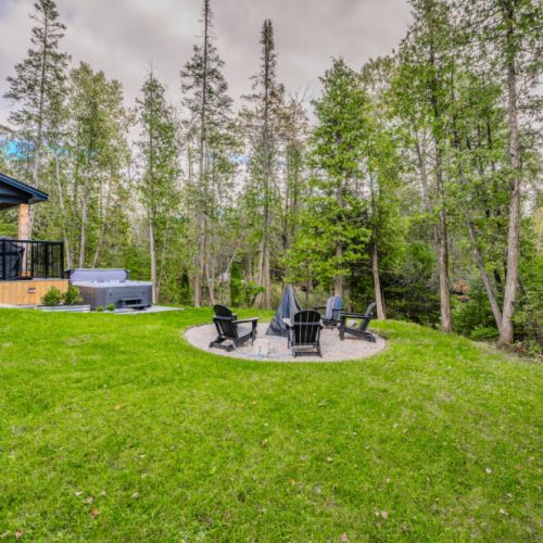 A beautiful backyard setting featuring a deck, hot tub, and a spacious fire pit area, ideal for outdoor leisure and enjoyment.