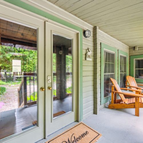 Unwind on the covered porch, featuring cozy Adirondack chairs, serene forest views, and charming French doors—perfect for morning coffee or evening relaxation during your peaceful Grey Bruce getaway.