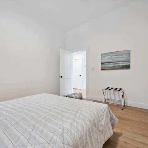 Bright, minimalist bedroom with comfortable queen bed, warm wood floors, and simple modern décor.