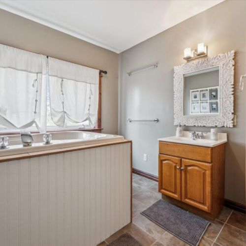 Upstairs bathroom with a large soaker tub, bright natural light, and decorative vanity mirror.